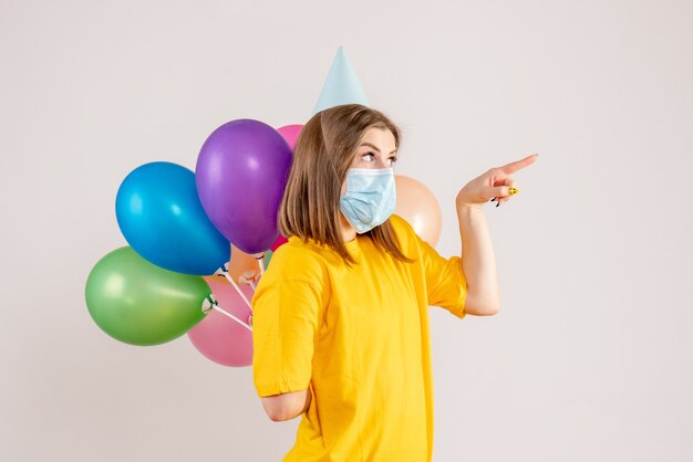 junge Frau, die bunte Luftballons hinter ihrem Rücken in der Maske auf Weiß versteckt