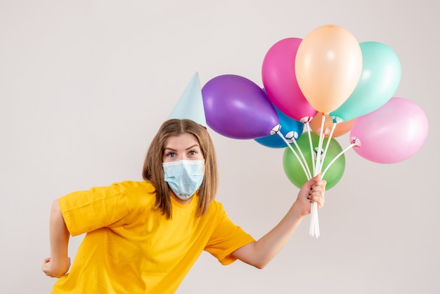 junge Frau, die bunte Luftballons in der Maske auf Weiß hält