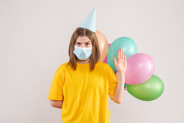 junge Frau, die bunte Luftballons in der Maske auf Weiß hält