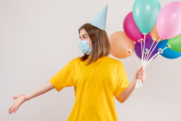 junge Frau, die bunte Luftballons in der Maske auf Weiß hält