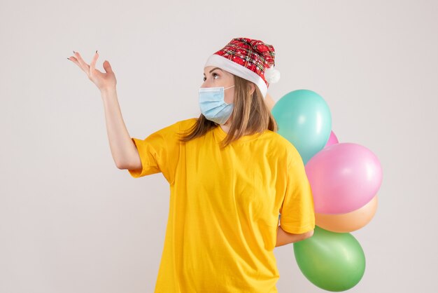 junge Frau, die bunte Luftballons in der Maske auf Weiß hält