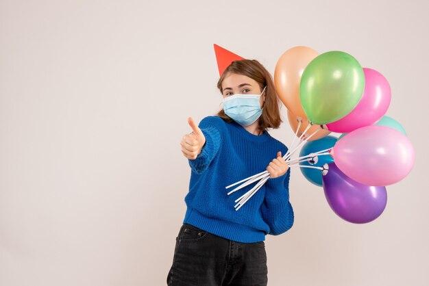 junge Frau, die bunte Luftballons in der Maske auf Weiß hält