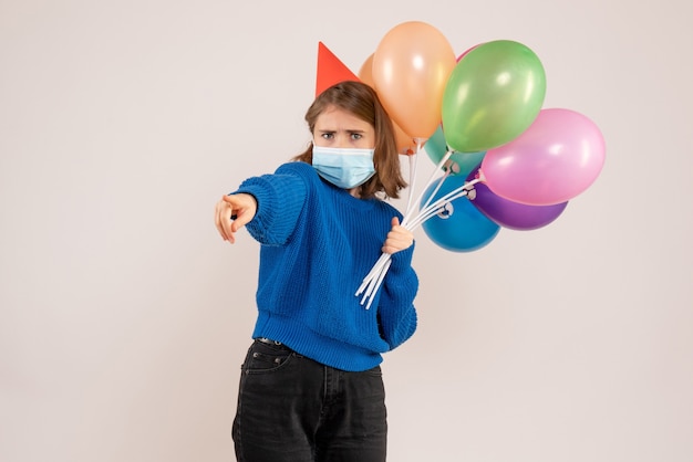 junge Frau, die bunte Luftballons in der Maske auf Weiß hält