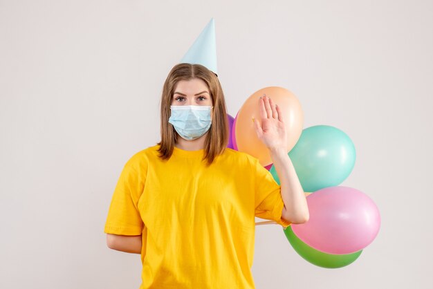 junge Frau, die bunte Luftballons in der Maske auf Weiß hält