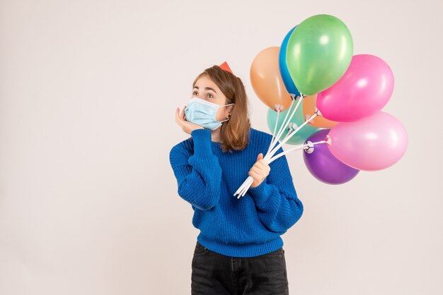 junge Frau, die bunte Luftballons in der Maske auf Weiß hält