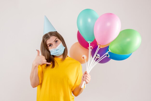 junge Frau, die bunte Luftballons in der Maske auf Weiß hält