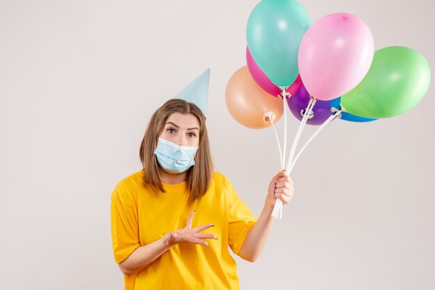 junge Frau, die bunte Luftballons in der Maske auf Weiß hält