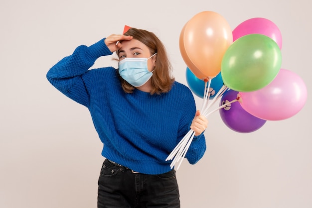 junge Frau, die bunte Luftballons in der Maske auf Weiß hält