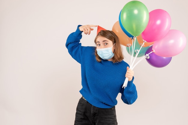 junge Frau, die bunte Luftballons in der Maske auf Weiß hält