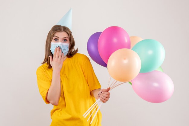 junge Frau, die bunte Luftballons in der Maske auf Weiß hält