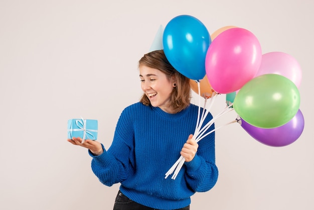 junge Frau, die bunte Luftballons und wenig Geschenk auf Weiß hält