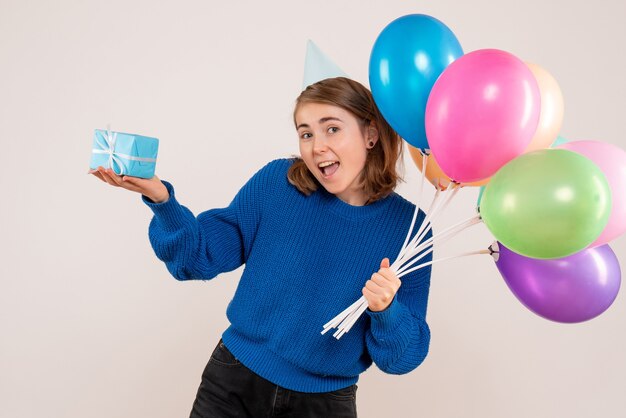 junge Frau, die bunte Luftballons und wenig Geschenk auf Weiß hält