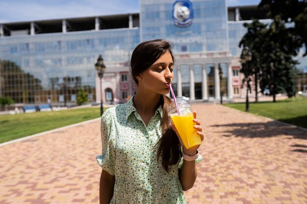 Junge Frau, die Cocktail mit Eis im Plastikbecher mit Strohhalm auf Stadtstraße lächelt und trinkt.