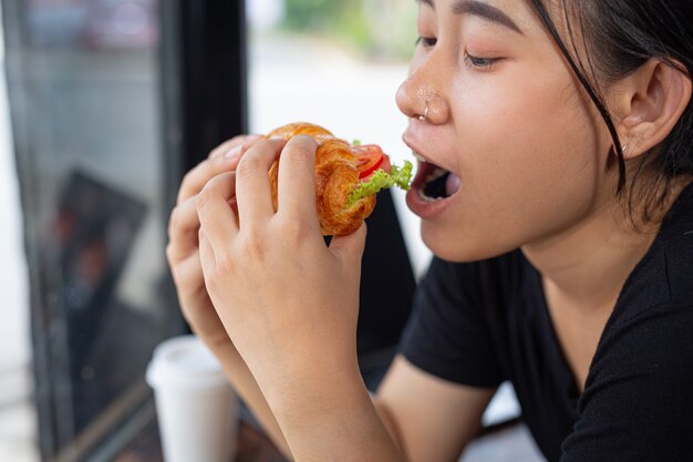 Junge Frau, die Croissant-Sandwiches im Büroraum isst