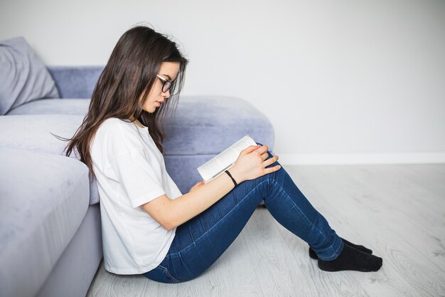 Junge Frau, die das Lesen nahe Sofa genießt