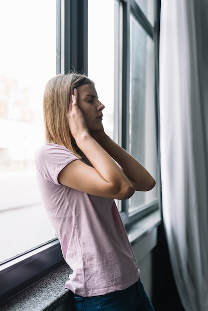 Junge Frau, die das nahe Fenster leidet unter Kopfschmerzen steht