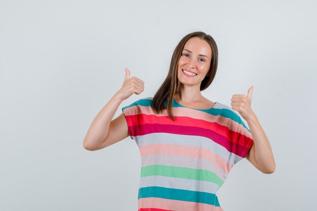 Junge Frau, die Daumen oben im T-Shirt zeigt und glücklich schaut. Vorderansicht.