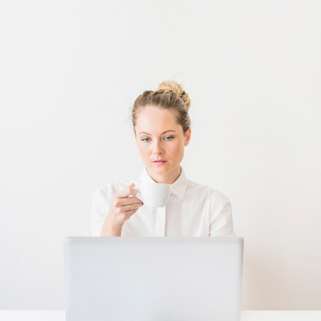 Junge Frau, die den Tasse Kaffee betrachtet Laptop hält