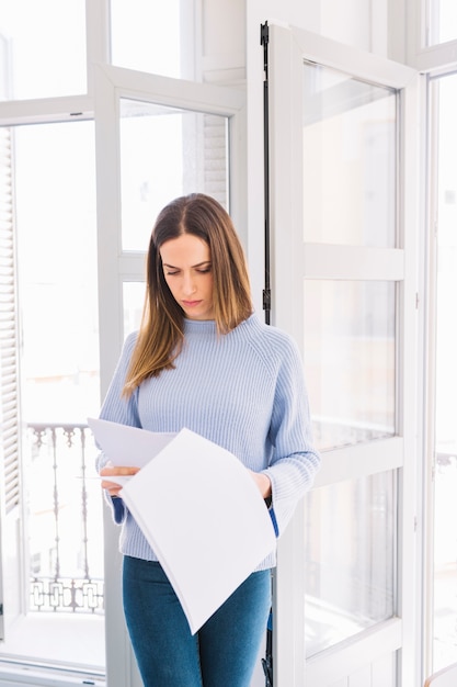 Junge Frau, die Dokumente nahe Fenster liest