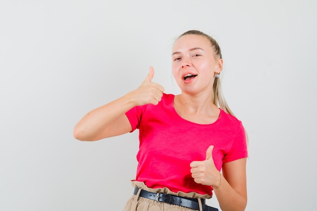 Kostenloses Foto junge frau, die doppelte daumen oben im t-shirt und in der hose zeigt und fröhlich aussieht