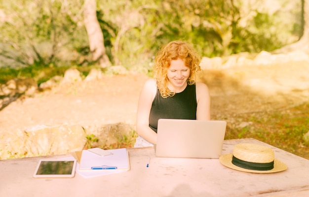 Kostenloses Foto junge frau, die draußen am schreibtisch sitzt und an laptop arbeitet