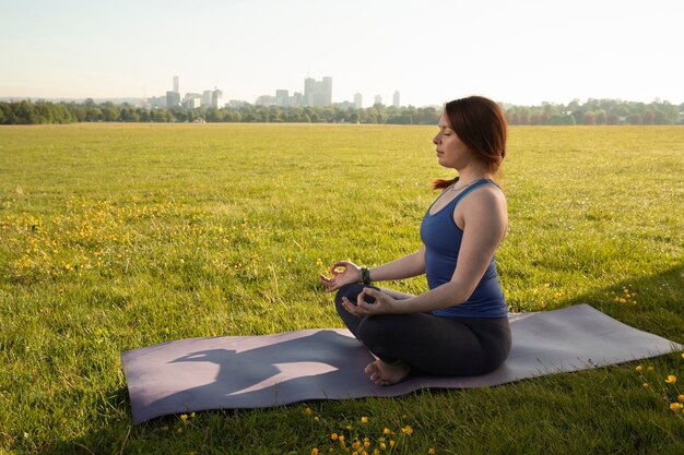 Junge Frau, die draußen auf Yogamatte meditiert
