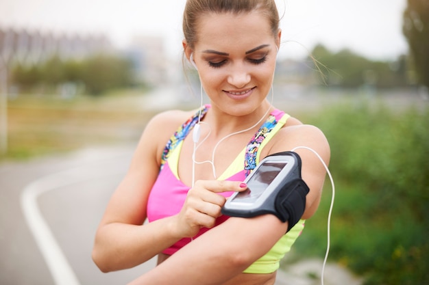 Junge Frau, die draußen trainiert. Einschalten einer Wiedergabeliste vor dem Joggen