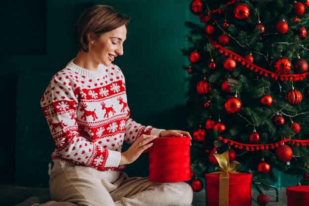 Junge Frau, die durch den Weihnachtsbaum mit roten Kästen sitzt