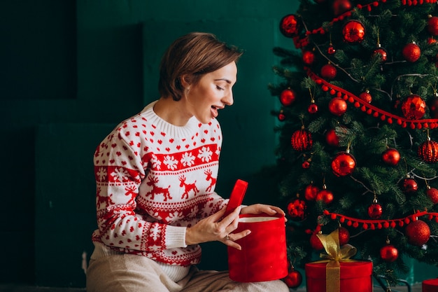 Junge frau, die durch den weihnachtsbaum mit roten kästen sitzt