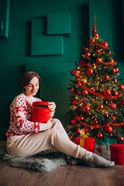 Junge Frau, die durch den Weihnachtsbaum mit roten Kästen sitzt