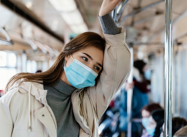 Junge Frau, die durch U-Bahn reist, die eine chirurgische Maske trägt