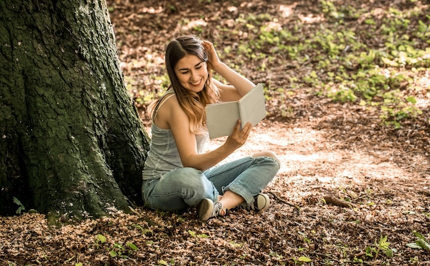 Junge Frau, die ein Buch nahe einem Baum liest