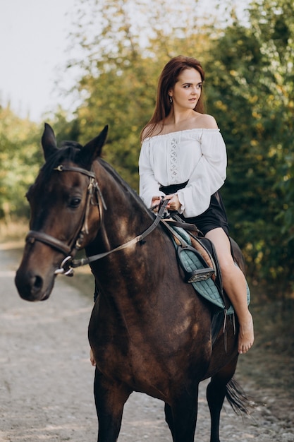 Junge Frau, die ein Pferd im Wald reitet