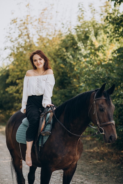 Junge Frau, die ein Pferd im Wald reitet