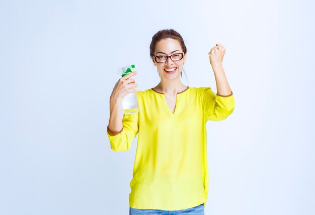 Junge Frau, die ein Reinigungsspray hält und Freudenzeichen zeigt