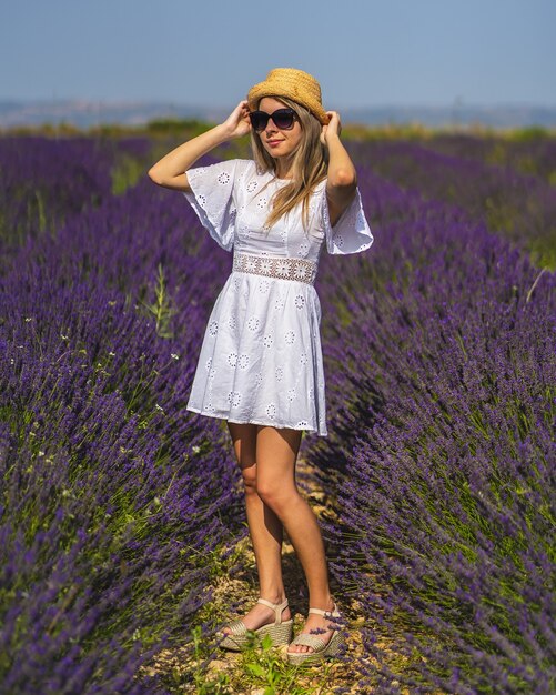 Junge Frau, die ein schönes Kleid trägt, das an einem sonnigen Tag in einem Lavendelfeld spaziert?