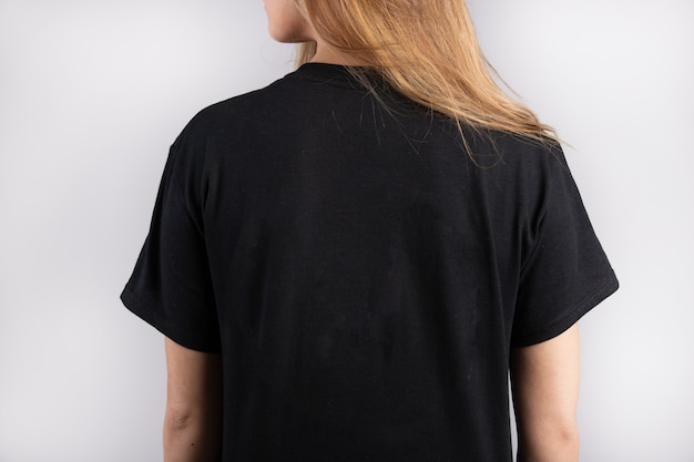 Junge Frau, die ein schwarzes kurzärmliges T-Shirt mit einer weißen Wand im Hintergrund trägt