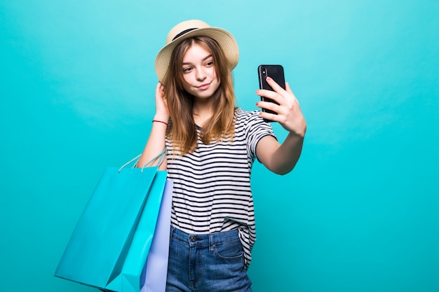 Junge Frau, die ein Selfie auf Ihrem Smartphone macht, das mit farbigen Taschen zum Einkaufen sitzt