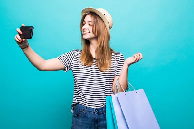 Junge Frau, die ein Selfie auf Ihrem Smartphone macht, das mit farbigen Taschen zum Einkaufen sitzt