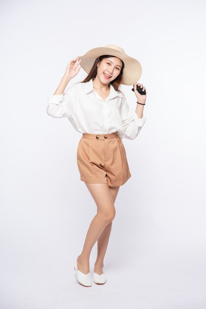 Junge Frau, die ein weißes Hemd und Shorts trägt, einen Hut und Griff auf dem Hut trägt