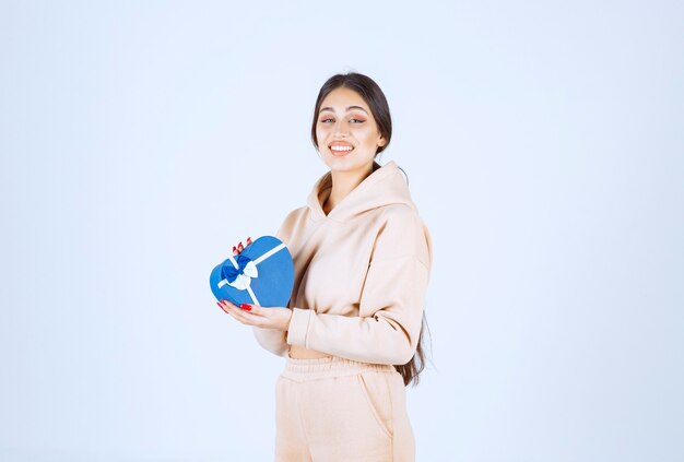 Junge Frau, die eine blaue Herzform-Geschenkbox hält und glücklich aussieht