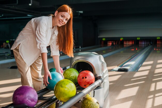 Junge Frau, die eine bunte Bowlingkugel nimmt