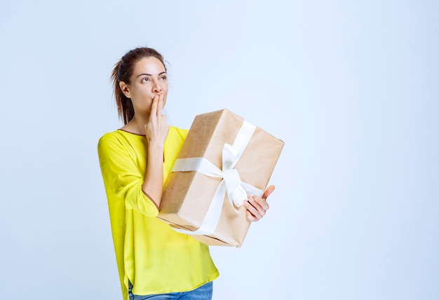 Junge Frau, die eine Geschenkbox aus Karton hält und an den unbekannten Absender denkt