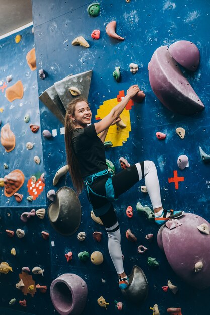 Junge Frau, die eine große, künstliche Kletterwand klettert