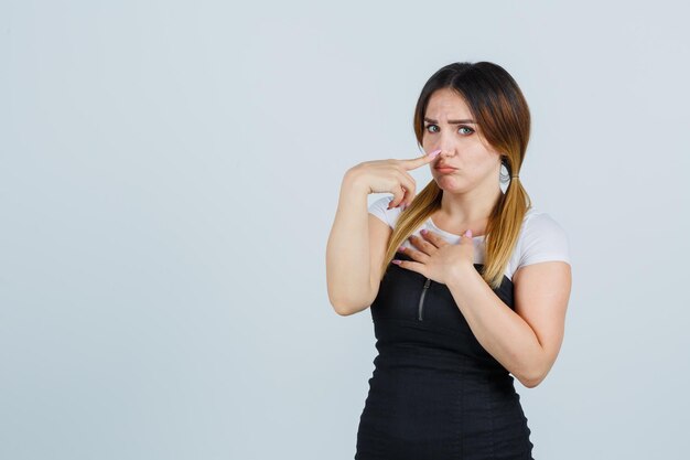 Junge Frau, die eine Hand über die Brust hält, während sie den Zeigefinger auf die Nase legt