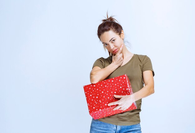 Junge Frau, die eine rote Geschenkbox hält und eine gute Idee hat