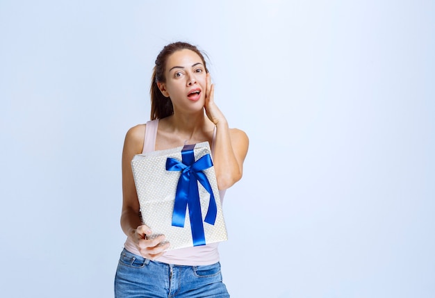 Junge Frau, die eine weiße Geschenkbox hält, die mit blauem Band umwickelt ist