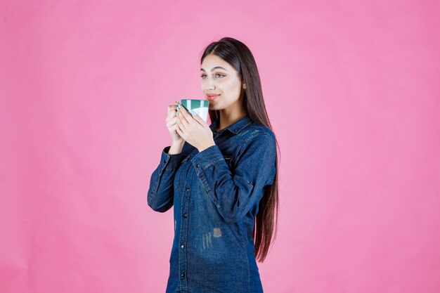 Junge Frau, die eine weiße grüne Kaffeetasse hält und riecht