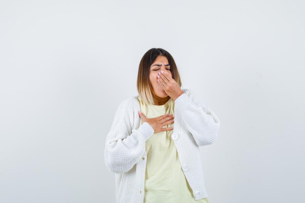 Junge Frau, die eine weiße Strickjacke trägt, gähnt