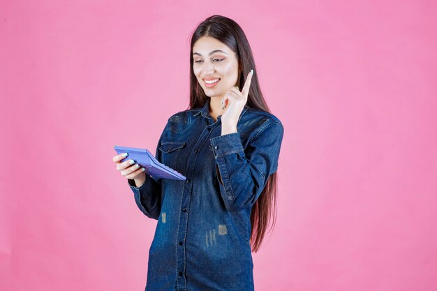 Junge Frau, die einen blauen Taschenrechner hält und denkt